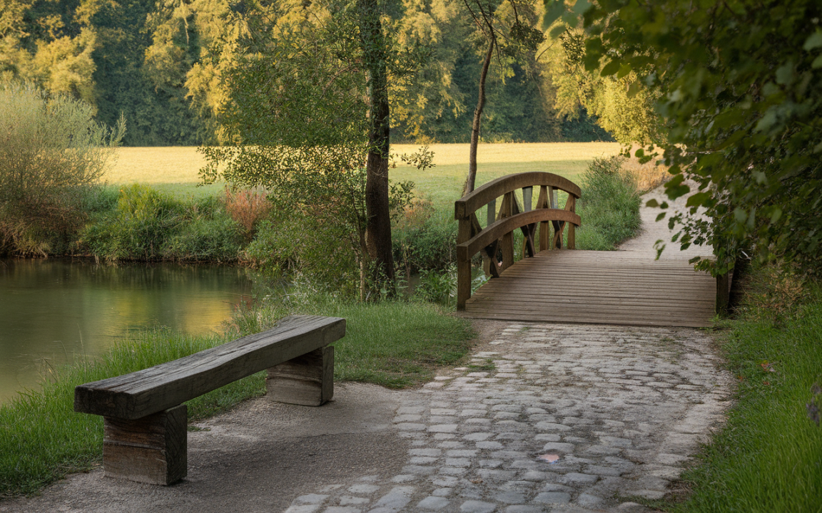 Un banc en bois sur un chemin de pierre, avec un pont en bois surplombant un cours d'eau, entouré de verdure.