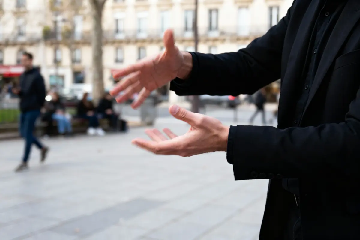 Gros plan sur des mains gesticulant, arrière-plan flou de personnes dans la rue.