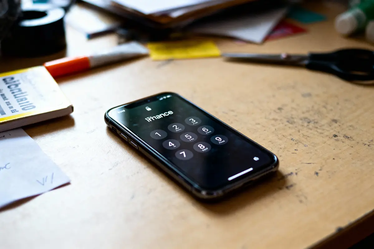 Smartphone affichant un écran de verrouillage avec pavé numérique, posé sur un bureau en désordre.