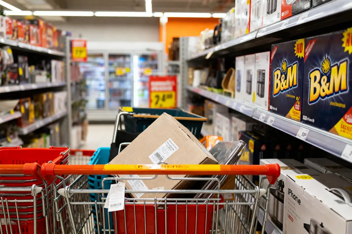 Chariot dans un magasin, rempli de boîtes et articles divers, rayons de produits ménagers autour.