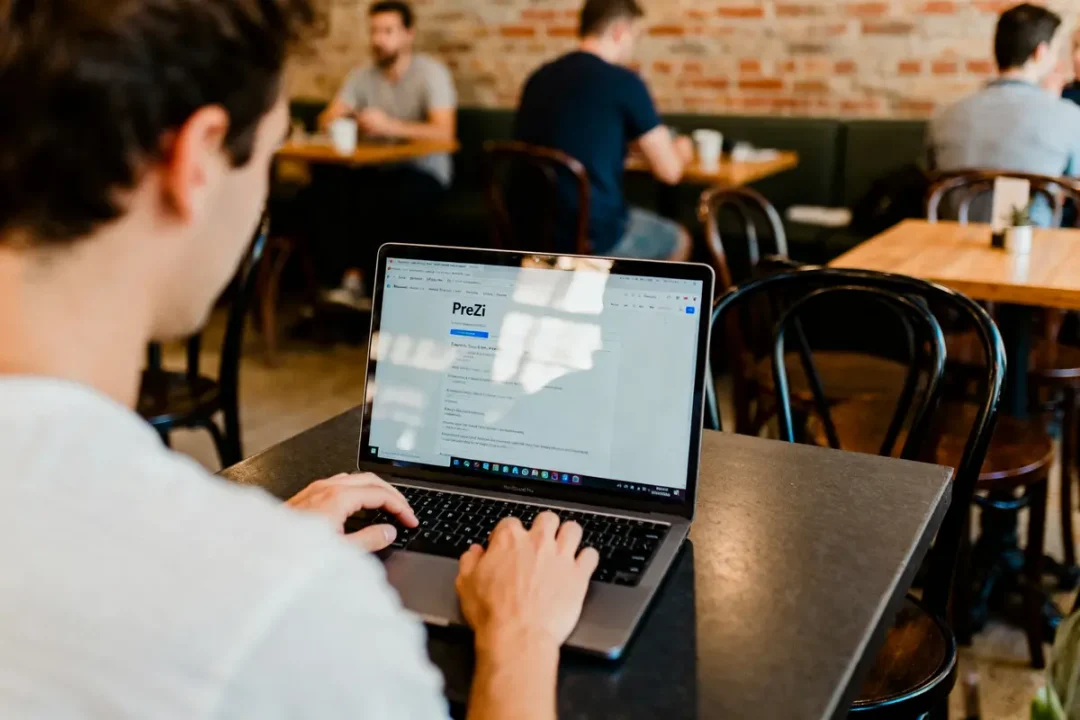 Personne utilisant un ordinateur portable dans un café avec d'autres clients en arrière-plan.