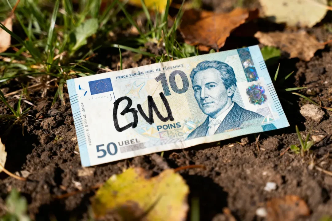 Billet de 50 Ubel fictif, avec visage masculin, marqué "BW", posé sur le sol herbeux.