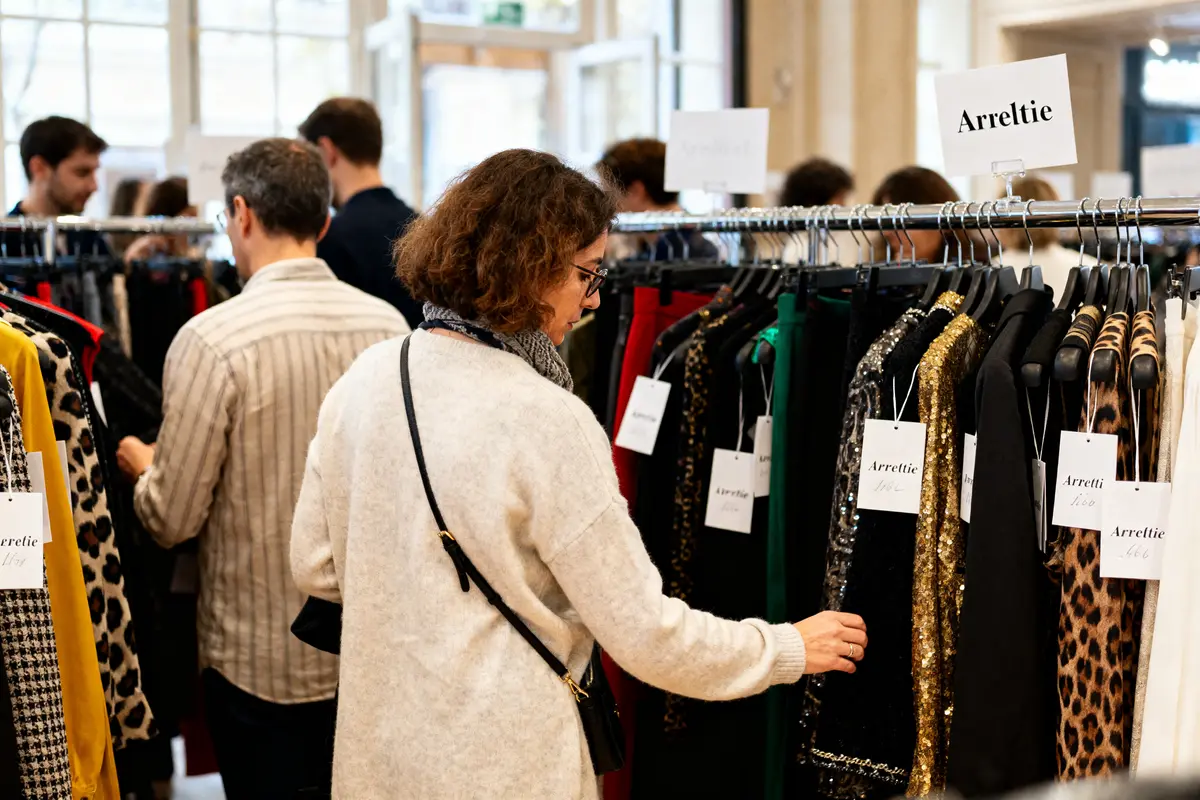Personnes explorant les vêtements Arlettie lors d'une vente en showroom avec étiquettes visibles