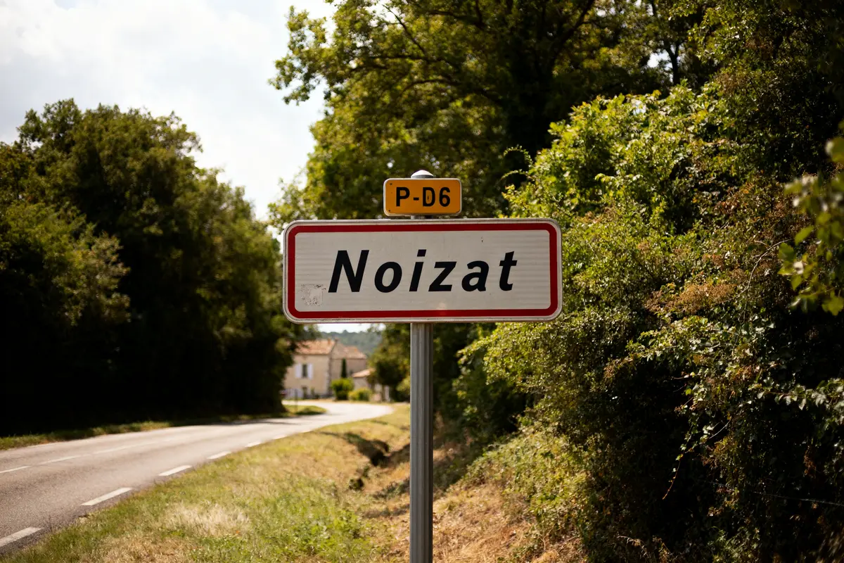 Panneau routier Noizat entouré d'arbres sur une route sinueuse campagnes.
