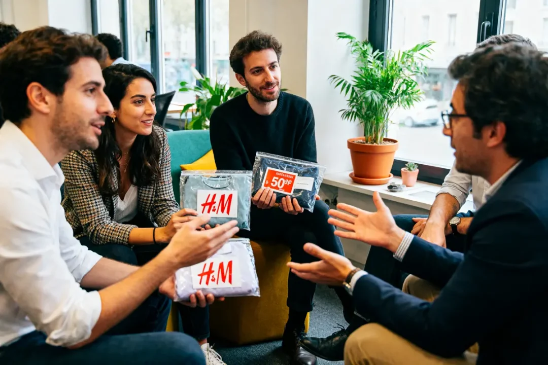 Quatre personnes discutent autour de vêtements H&M, dans une salle avec des plantes.