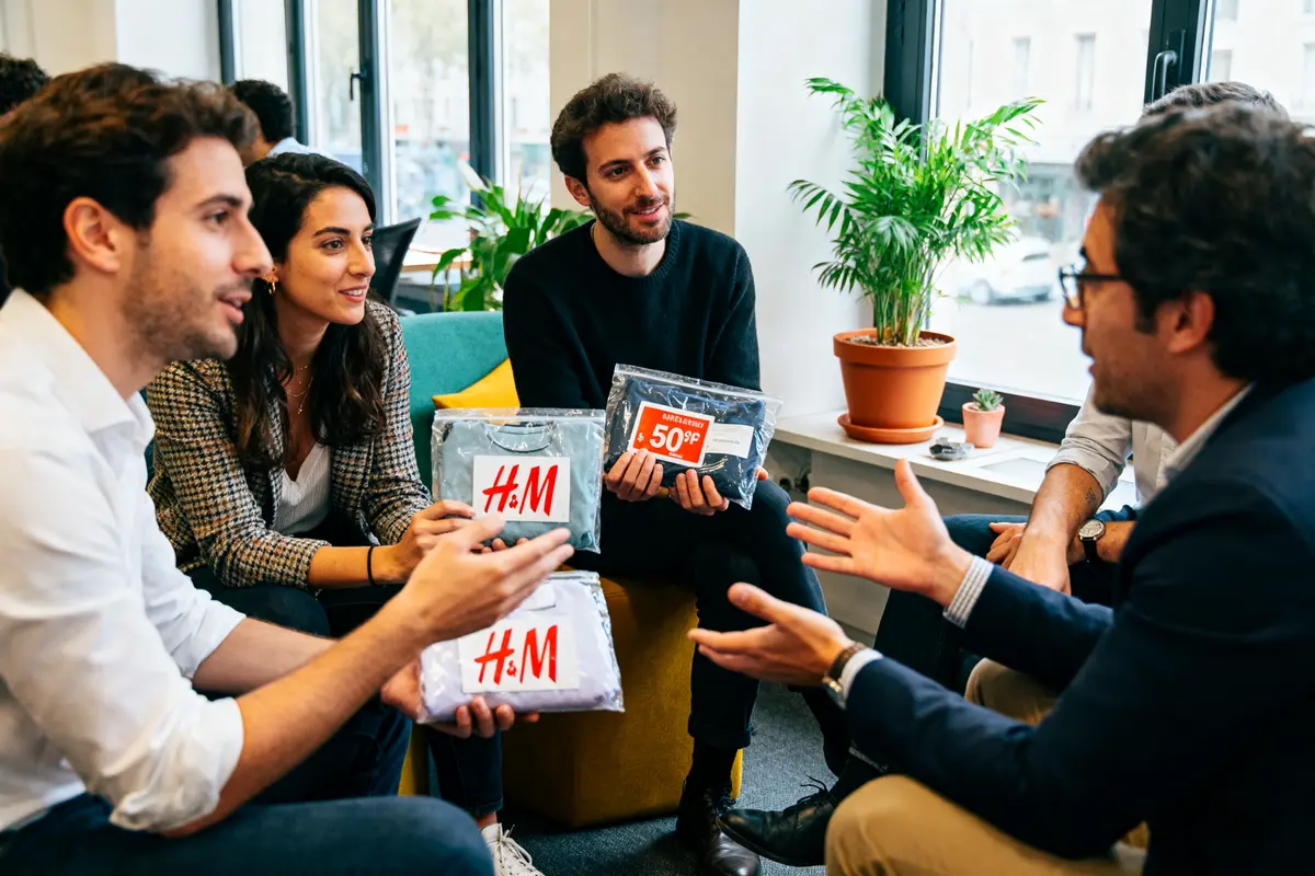 Quatre personnes discutent autour de vĂŞtements H&M, dans une salle avec des plantes.