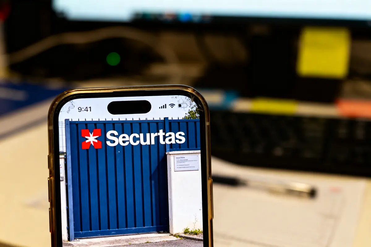 Smartphone affichant portail Securitas, posé devant un clavier et écran d'ordinateur flous.