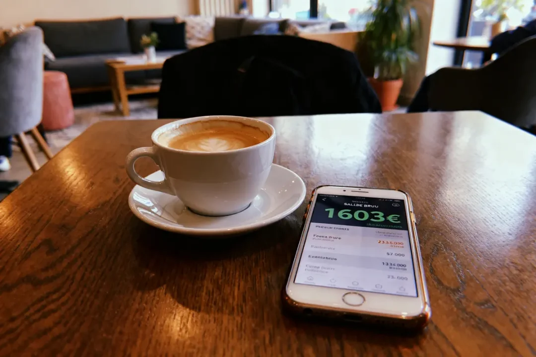 Tasse de café avec smartphone affichant 1603€ brut convertis en net sur table de café