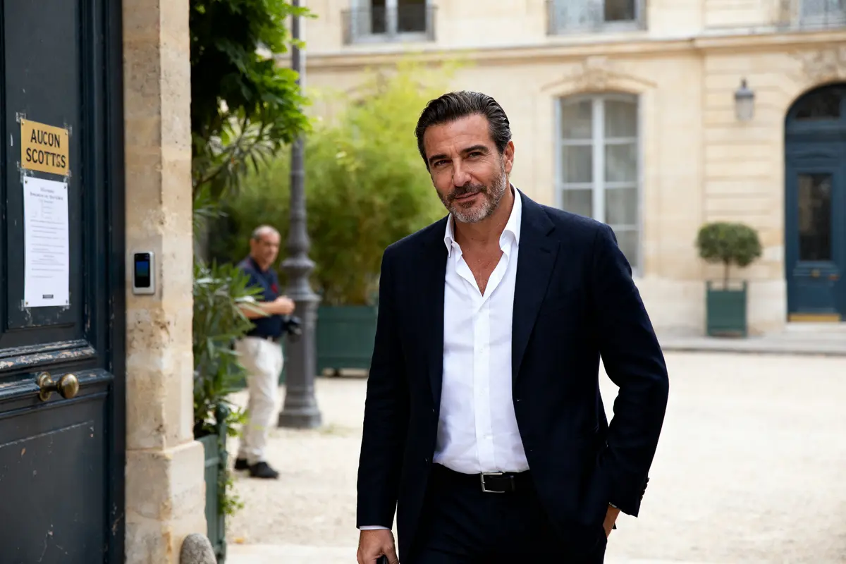 Homme en costume souriant devant un bâtiment évoquant la fortune de Tony Scotti