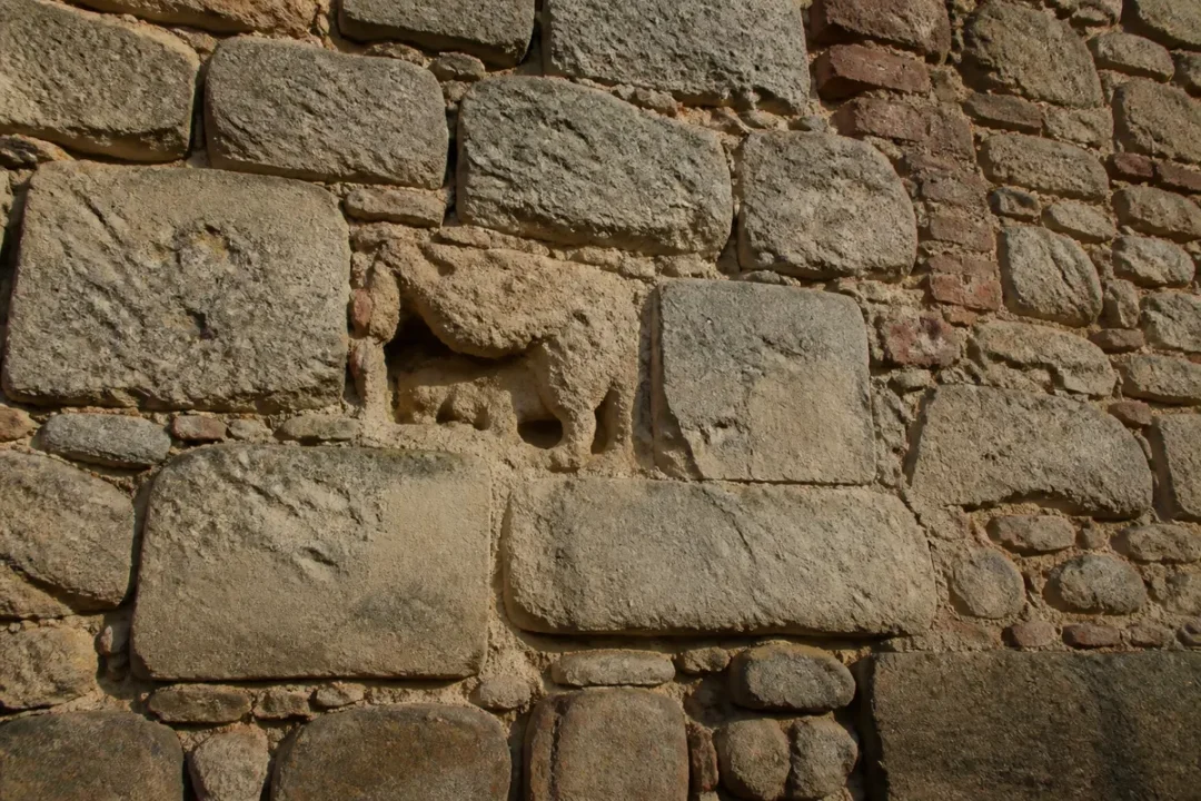 Mur de pierre ancienne avec sculpture d'animal intégré, lumière naturelle, texture brute et irrégulière.