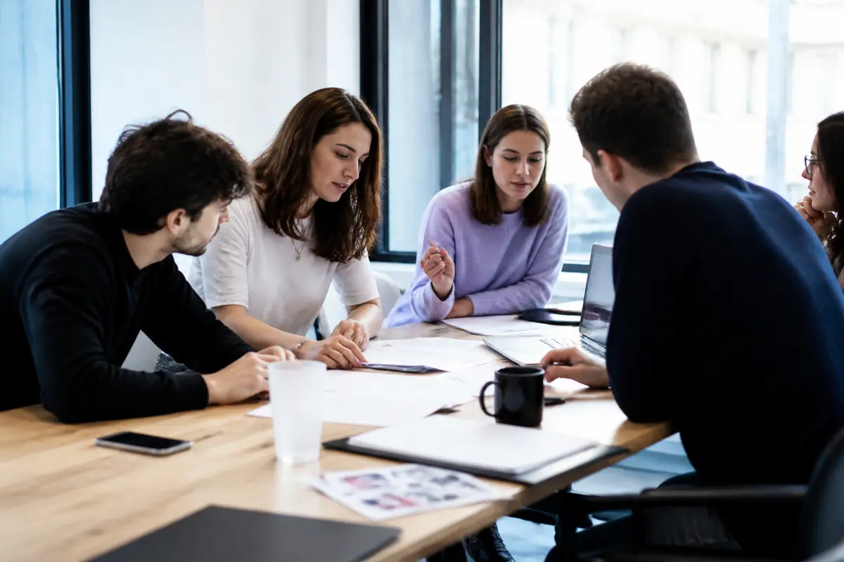 Un groupe de personnes discute autour d'une table avec des documents et un ordinateur portable.