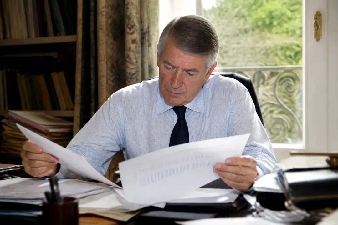 Un homme examinant des documents à son bureau près d'une fenêtre ensoleillée.