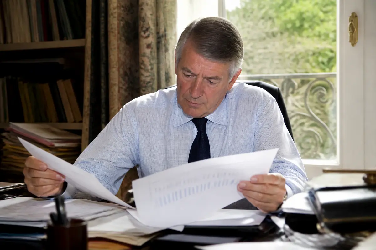 Un homme examinant des documents à son bureau près d'une fenêtre ensoleillée.