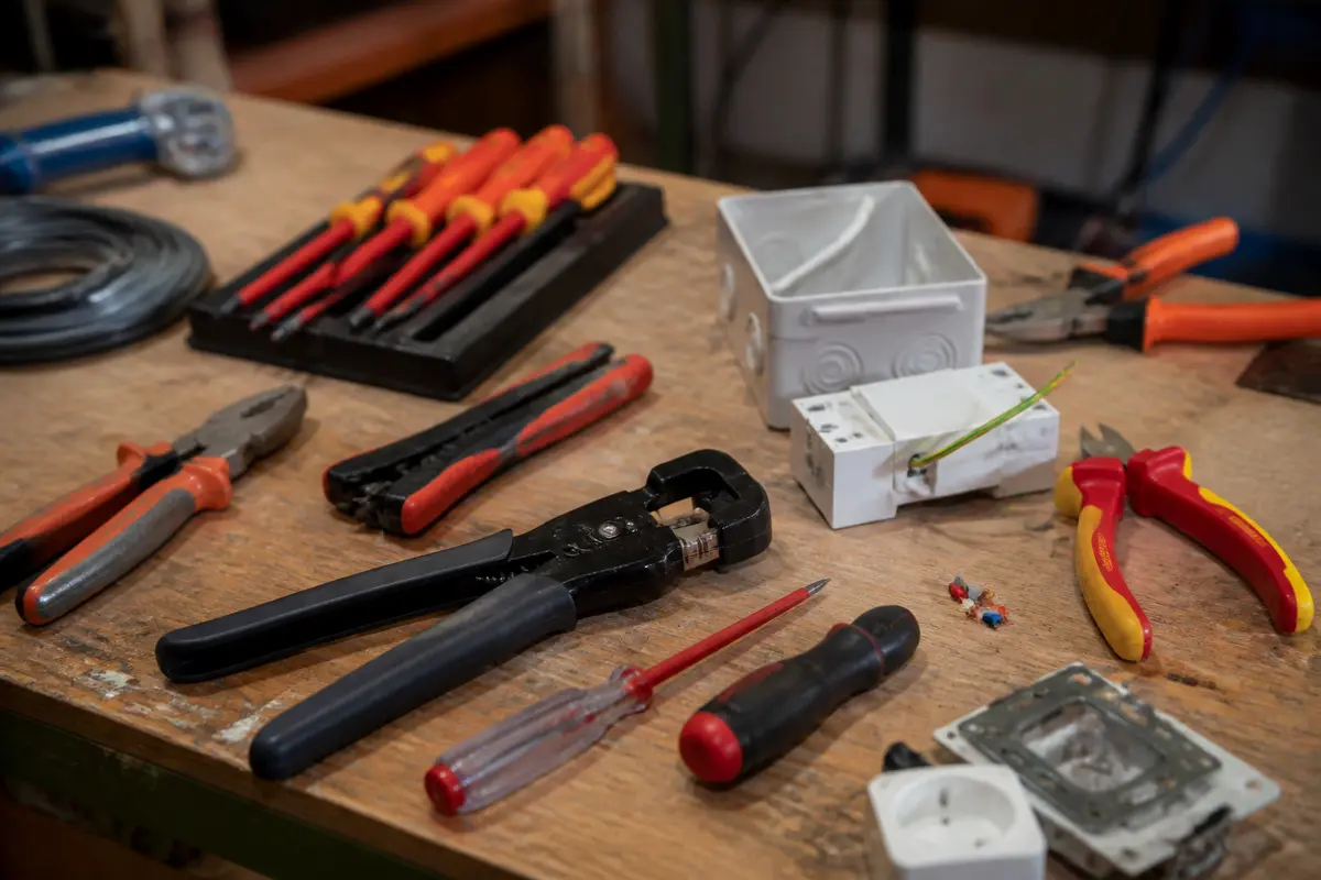 Plan de travail avec outils d'électricien, pinces, tournevis, fils électriques, boîte de raccordement.