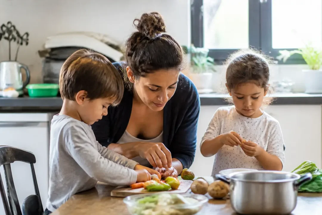 Une femme et deux enfants préparent des légumes ensemble dans une cuisine lumineuse.