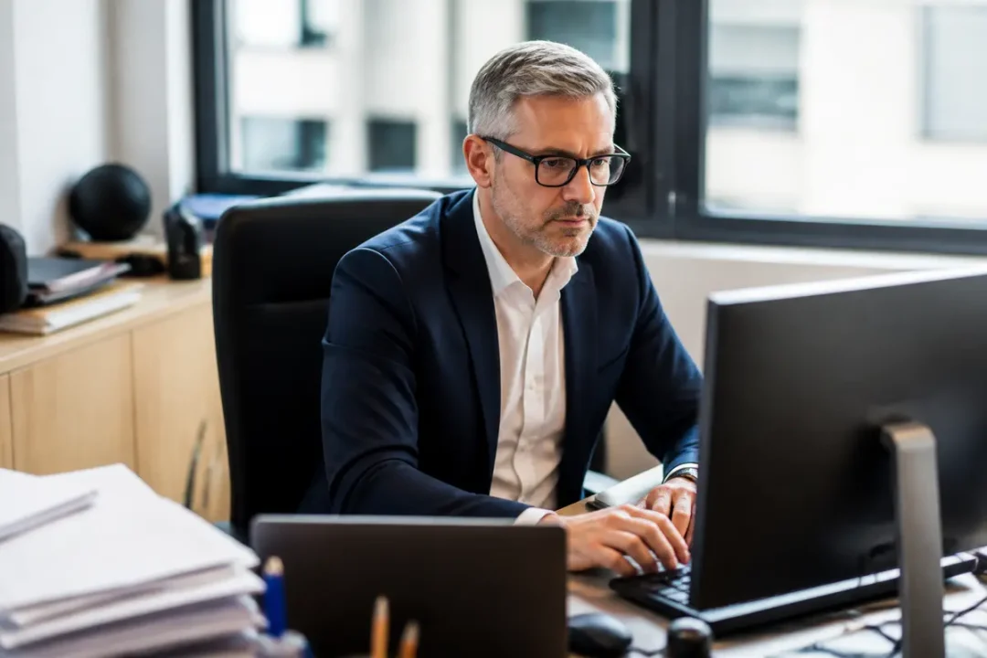 Homme à lunettes travaillant sur ordinateur dans un bureau moderne et lumineux.